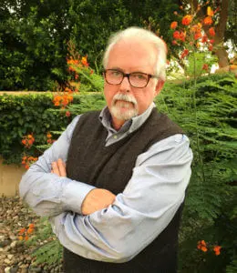 A man with glasses and beard standing in front of trees.