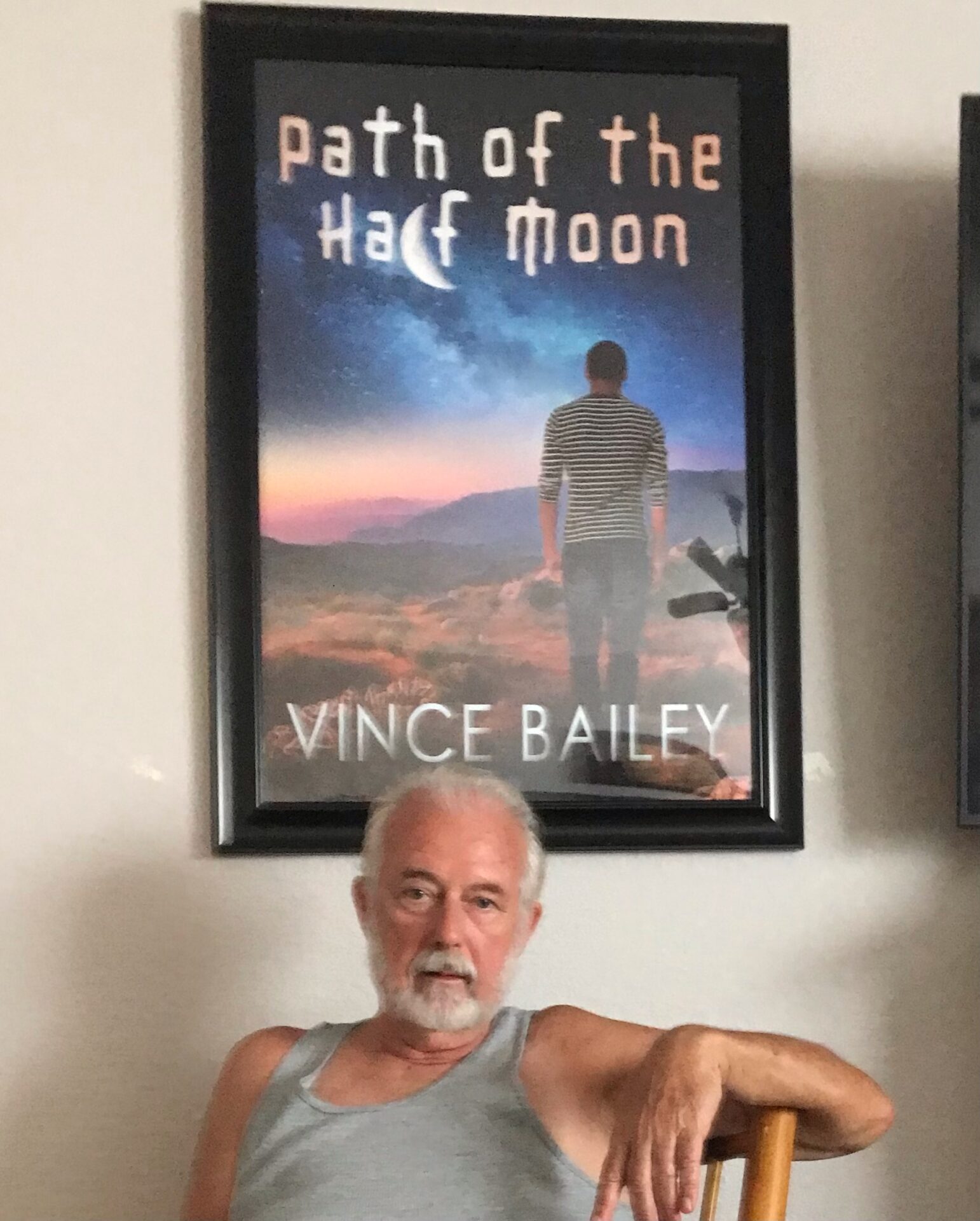 A man sitting in front of a poster of the book path of the half moon.